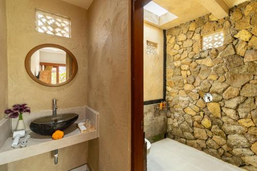 a bathroom with a sink and a stone wall at Ubud Heritage Stay by Dhananjaya Hospitality in Ubud