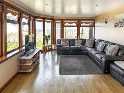 a living room with a black leather couch and a television at Maple Cottage in Inverallochy