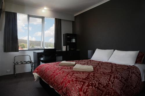 1 dormitorio con 1 cama con manta roja y ventana en White Manor Motel, en Cooma