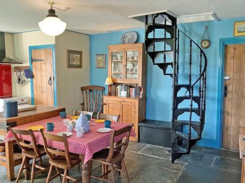 a dining room with a table and a spiral staircase at Downhouse in Delabole