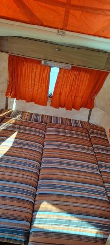 a bed in the back of a bus with orange curtains at Chez Flo&Fred Caravane Vintage in Barbery