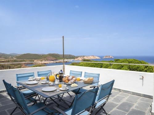 a table with chairs and food on a balcony with the ocean at Villa Sa Blanca by Interhome in Es Mercadal