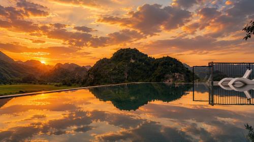 a swimming pool with a sunset in the background at Hotel LaVue Tam Coc in Ninh Binh