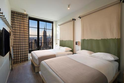 two beds in a room with a large window at Moxy NYC Chelsea in New York