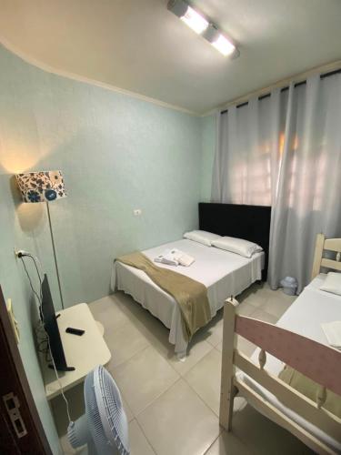 a bedroom with two beds and a desk with a fan at Pousada Allmar in Bertioga