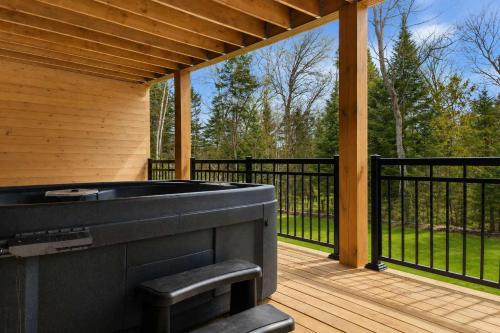 a hot tub on a wooden deck with a black fence at Spa - River - Game Room - Le Belvedere in Mont-Tremblant