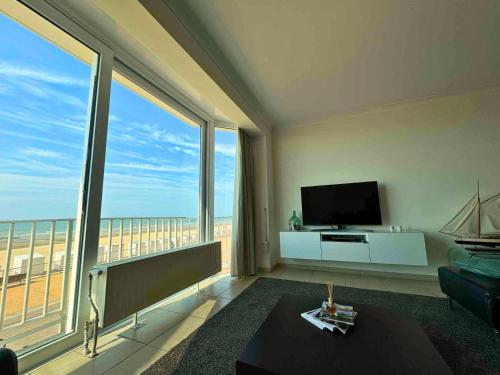 a living room with a television and large windows at Le Channel - Parenthèse calme face à la mer sur la digue - Idéal famille - Équipements bébé - Ascenseur in Koksijde