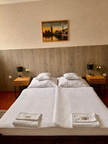 a bedroom with a large white bed with two tables at Muskátli Panzió és Étterem in Újhartyán