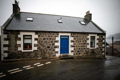 a brick house with a blue door on a street at Castle Grant - 4 Bed Cottage in Gardenstown in Gardenstown