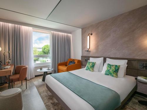 a hotel room with a bed and a desk and a window at Novotel Nice Aéroport Cap 3000 in Saint-Laurent-du-Var