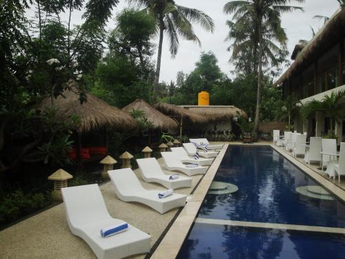 a row of white lounge chairs next to a swimming pool at Trawangan Nirvana in Gili Trawangan
