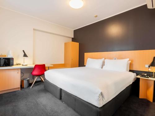 a hotel room with a large bed and a red chair at ibis Sydney World Square in Sydney