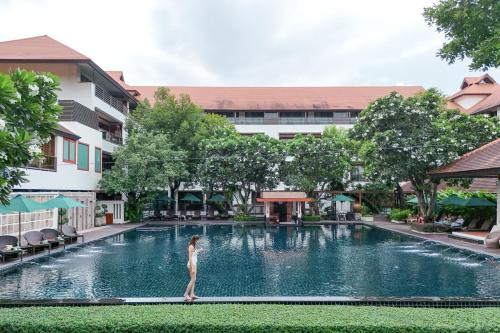 a woman standing on the edge of a swimming pool at a hotel at RatiLanna Riverside Spa Resort in Chiang Mai
