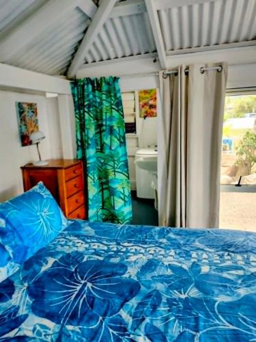 a bedroom with a blue bed and a bathroom at Heron's Reef Beach Shack Matavera in Matavera