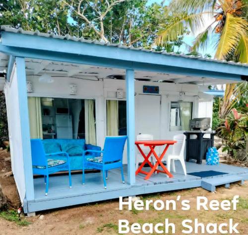 a beach shack with blue chairs and a red table at Heron's Reef Beach Shack Matavera in Matavera