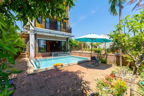 a house with a swimming pool and an umbrella at Calm House 4 Hoi An in Hoi An