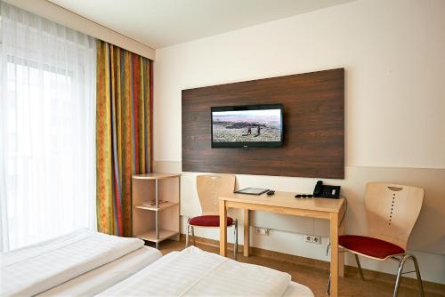 a hotel room with a desk and a tv on the wall at Hotel Kolping Wien Zentral in Vienna