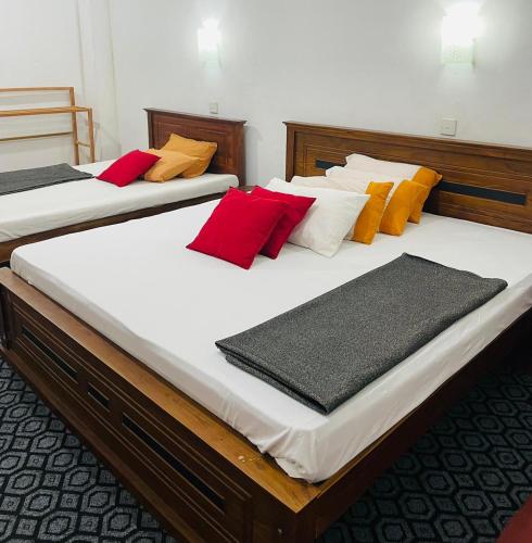 two beds in a room with red and yellow pillows at Madhusha Rest in Maskeliya