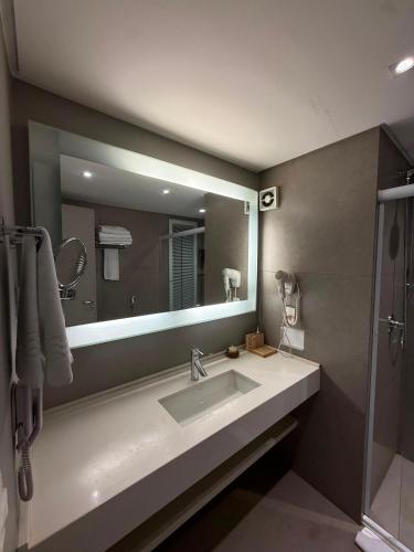 a bathroom with a sink and a large mirror at Lindo Flat Part Grand Mercure Varanda aconchegante in Brasília