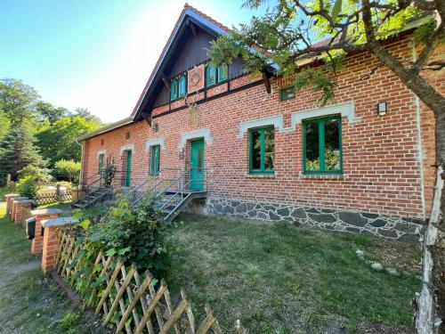 a brick house with green doors and a fence at Försterei Kalkhorst Ferienhaus am Naturschutzgebiet mit großem Garten in Neustrelitz