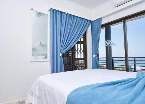 a bedroom with a bed with blue curtains and a window at Luxury Ocean View Escape with Private Rooftop -Sancta Maria in Kingsborough