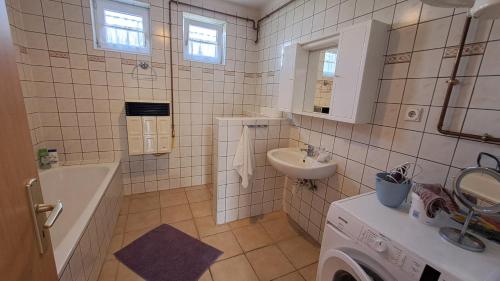 a white tiled bathroom with a sink and a bath tub at Mecseki Farkasvár in Magyarhertelend