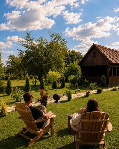 a man and a woman sitting in chairs in a yard at Căsuța cu tihnă in Porumbacu de Sus