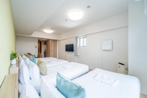 a room with four white beds with blue pillows at ESLEAD HOTEL Namba South Ⅲ in Osaka