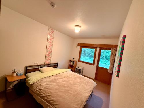 a bedroom with a bed and a table and two windows at Wakaranai Lodge Tomamu in Shimukappu