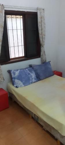 a bed with blue pillows in a room with a window at Casa Próximo Centro Itanhaém in Itanhaém