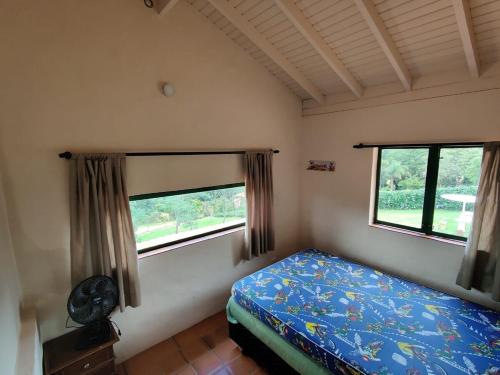 a small bedroom with a bed and two windows at Rancho Batatas in Atibaia