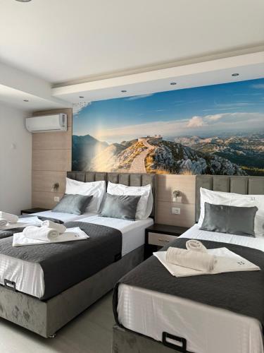 two beds in a room with a mountain mural on the wall at Apartments Vé in Budva