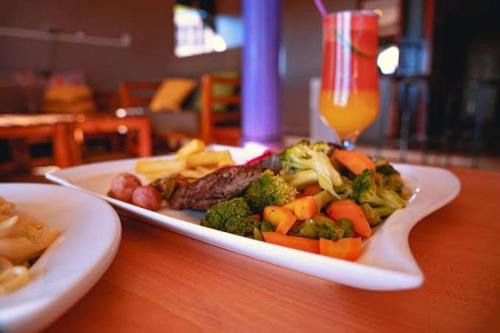 a plate of vegetables on a table with a drink at Golden Quest Hotel in Entebbe