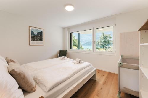 a white bedroom with a bed and two windows at FLORA BAY Spacious Lake and Mountain View Apartment in Niederried