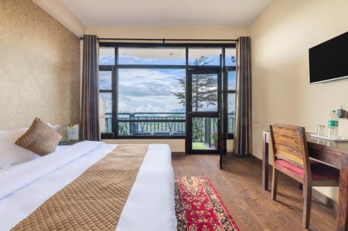 a bedroom with a bed and a desk and a large window at AyurVeda Haven Shimla l Pure Veg l l Lift l Power Backup l Multi Cuisine Restaurant l Free Parking l By Exotic Stays in Kūfrī