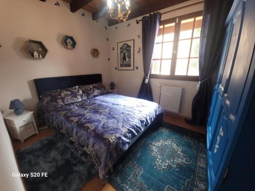 a bedroom with a bed with a blue comforter and a window at La symphonie des oiseaux in Villelongue-dʼAude