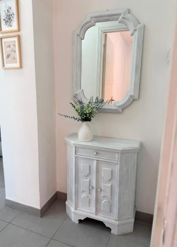 a white cabinet with a mirror and a vase with flowers at I Due Gelsi appartamento Green in Monte San Giusto