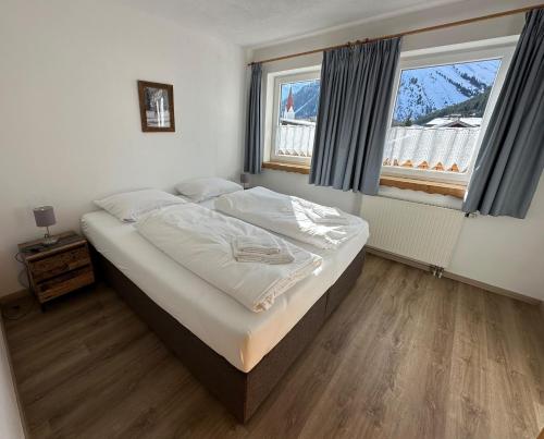 a bedroom with a bed with white sheets and two windows at Landhaus Cornelia in Berwang