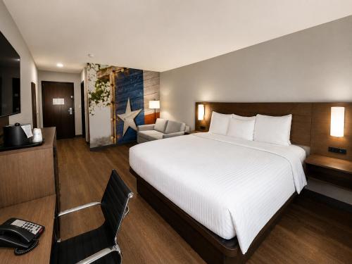 a hotel room with a large bed and a chair at Clarion Pointe Addison - Dallas North in Addison