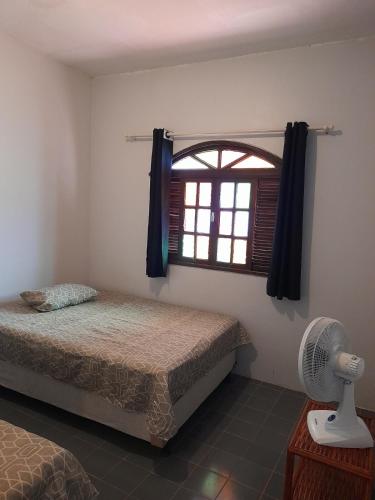 a bedroom with a bed and a window with a fan at Casa Vilarejo in Arembepe