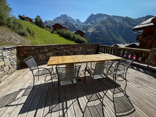 a wooden table and chairs on a deck with mountains at Black Diamond Sainte Foy Chalets in Sainte-Foy-Tarentaise