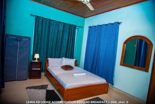 a bedroom with a bed with blue walls and a mirror at Le Mia KD lodge in Sekondi-Takoradi