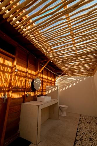 a bathroom with a toilet and a wooden ceiling at Westwood Bungalow in Gili Trawangan