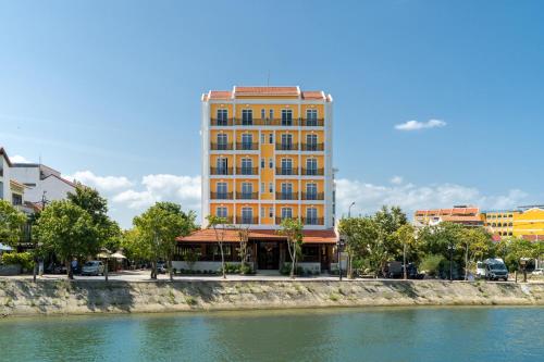 a tall yellow building next to a river at Royal Riverside Hoi An Hotel-Newly Renovated & Reopened in Hoi An