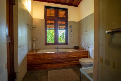 a bathroom with a tub and a toilet and a window at Jim's Farm Villas in Madawala