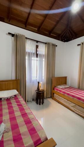 a bedroom with two beds and a table and a window at Rest Harrow Estate in Kandy
