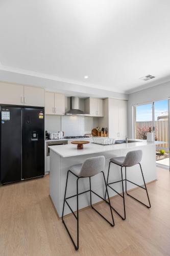 a kitchen with a black refrigerator and two bar stools at Alkimos Coastal Escape in Alkimos