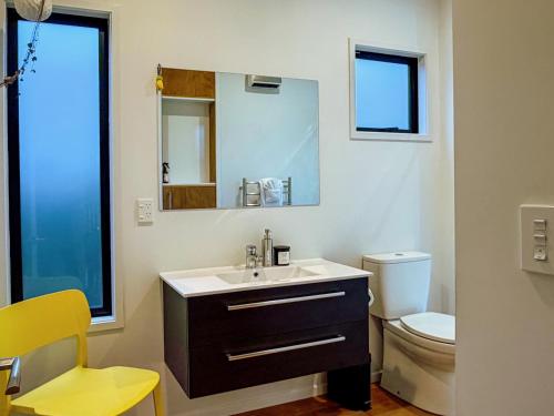 a bathroom with a sink and a toilet and a mirror at Kowhai Cabin - Serene Scandi Escape in Hokitika in Hokitika