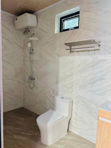 a white bathroom with a toilet and a window at Hoi An Ocean Waves Homestay in Hà My Tây (2)