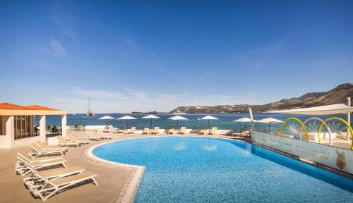 a swimming pool with chairs and the ocean in the background at Remisens Hotel Epidaurus-All inclusive in Cavtat